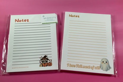 Two Halloween-themed notepads with cute illustrations on a pink background
