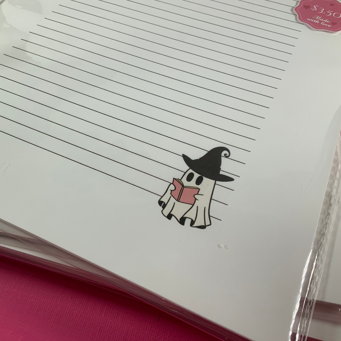 Notebook with a ghost wearing a witch hat and holding a pink heart on a pink background