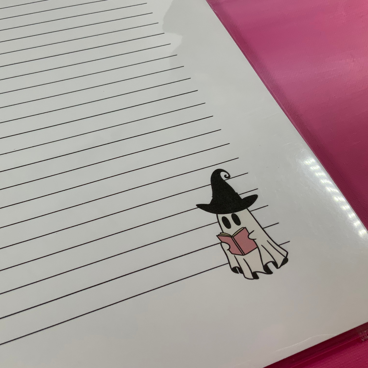 Notebook with a ghost in a witch hat and cape on lined paper, pink cover.