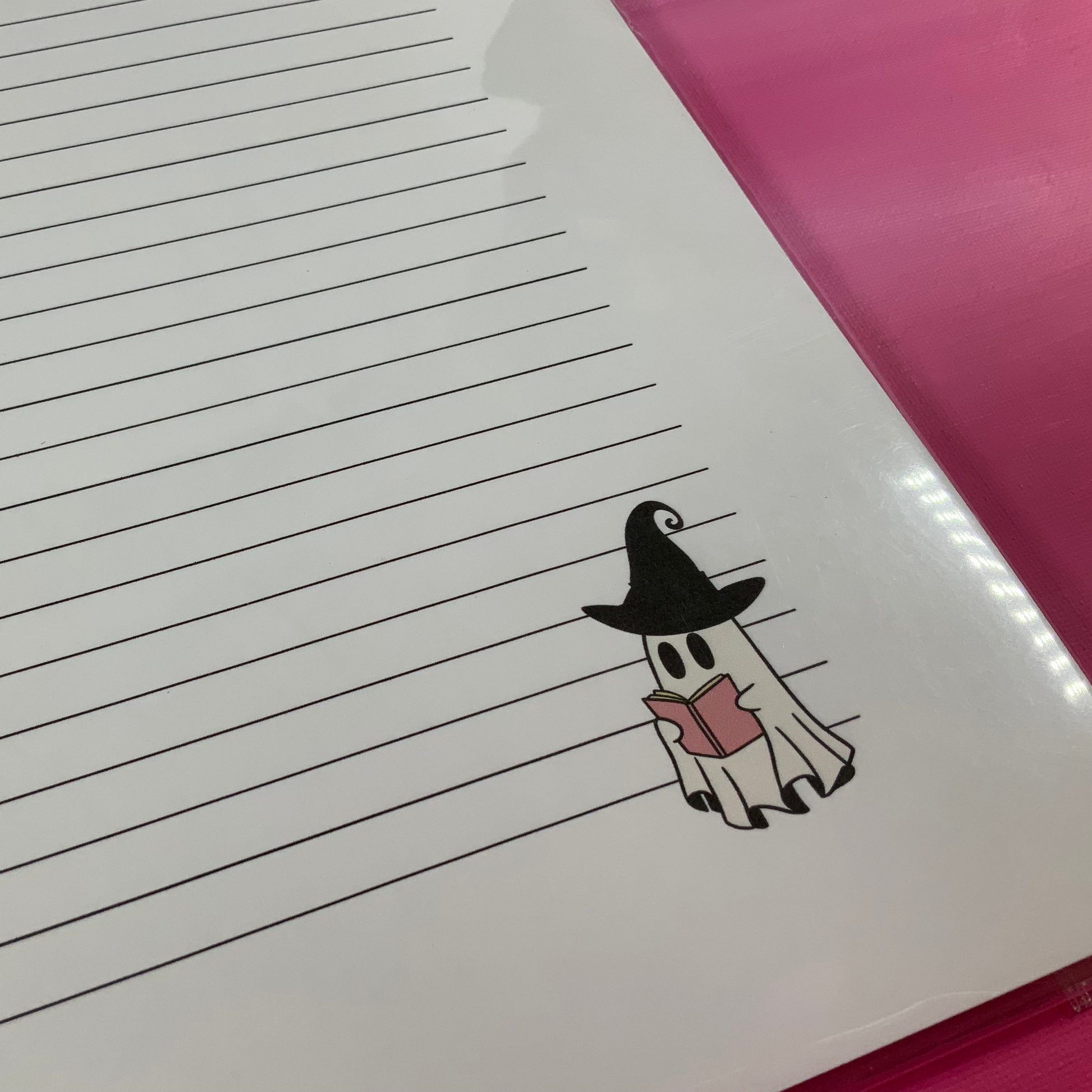 Notebook with a ghost in a witch hat and cape on lined paper, pink cover.