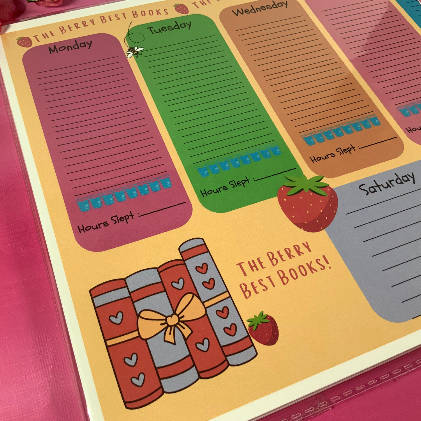 Weekly planner with days of the week and cartoon books on a pink surface