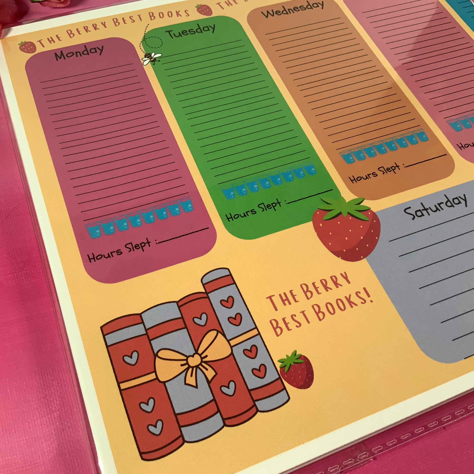 Weekly planner with days of the week and cartoon books on a pink surface