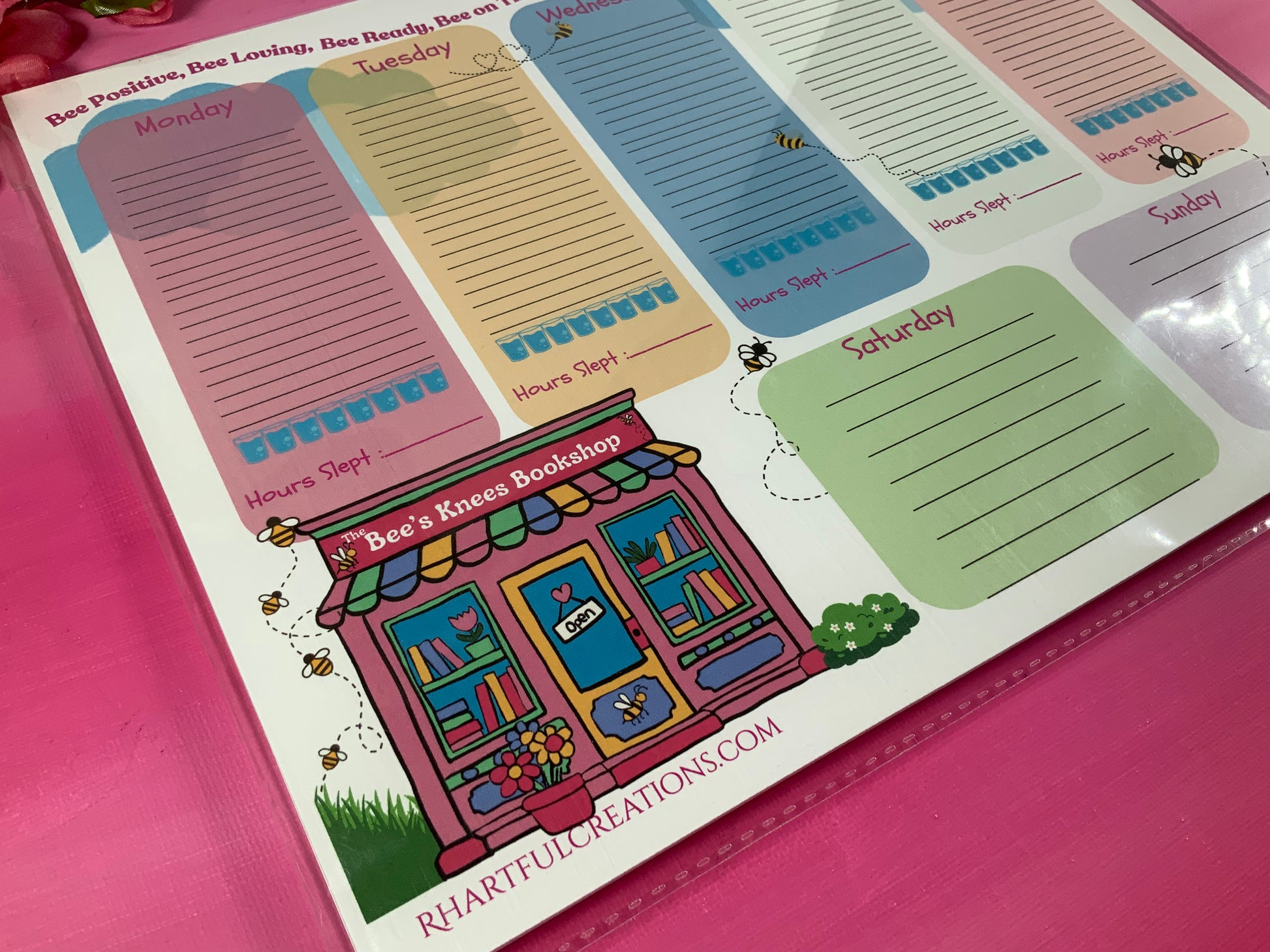 Weekly planner with colorful days of the week and a cartoon bookstore illustration on a pink background.