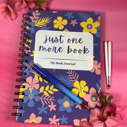 Notebook with floral design and 'just one more book' text on a pink background