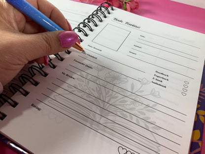 Hand holding a blue pen over a spiral-bound notebook with a floral design on a colorful background
