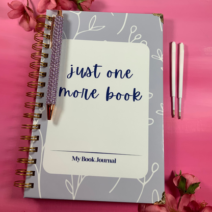 Notebook titled 'Just One More Book' with a pen on a pink background