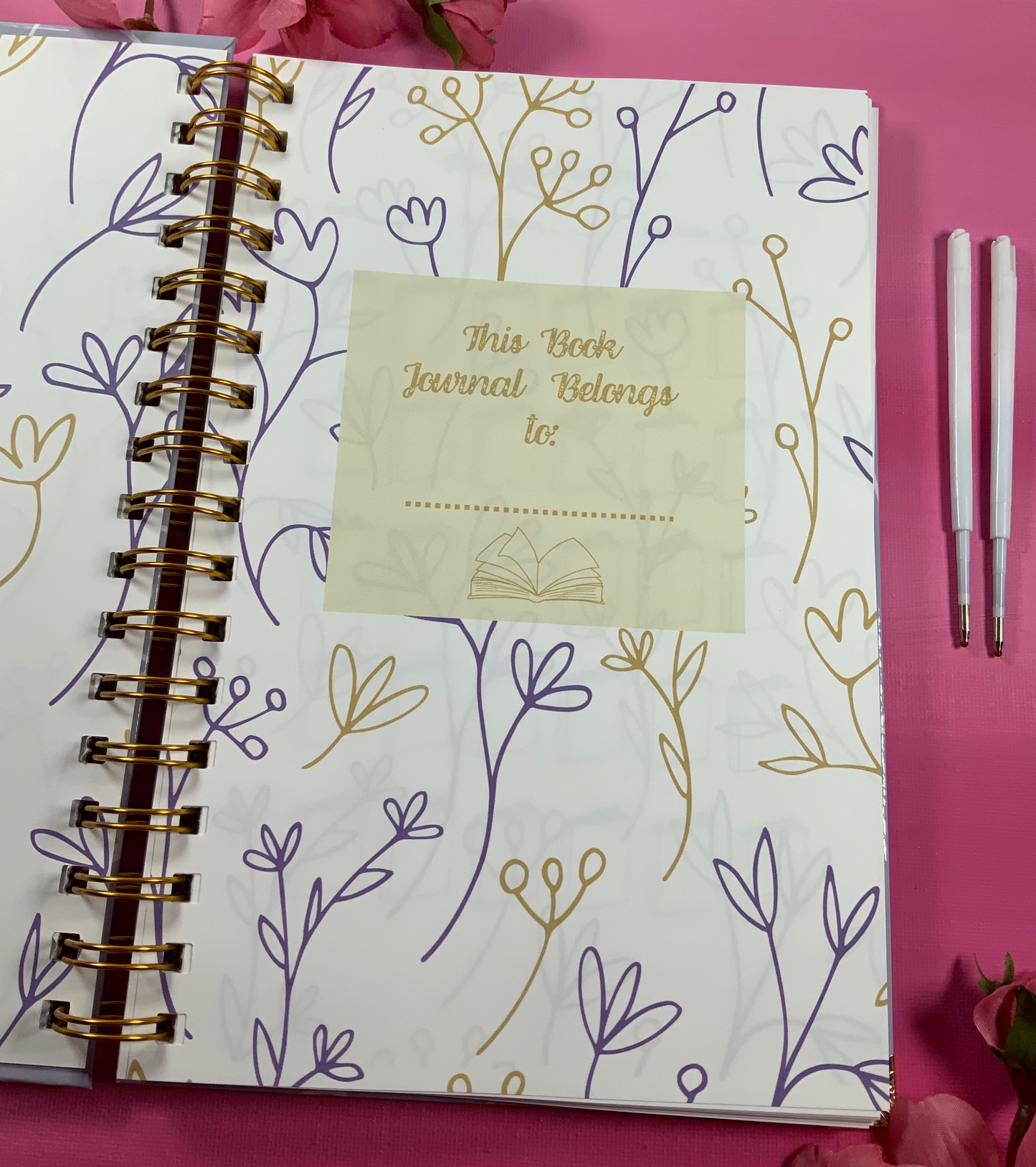 Journal with floral design and 'This Book Journal Belongs to' tag on a pink background