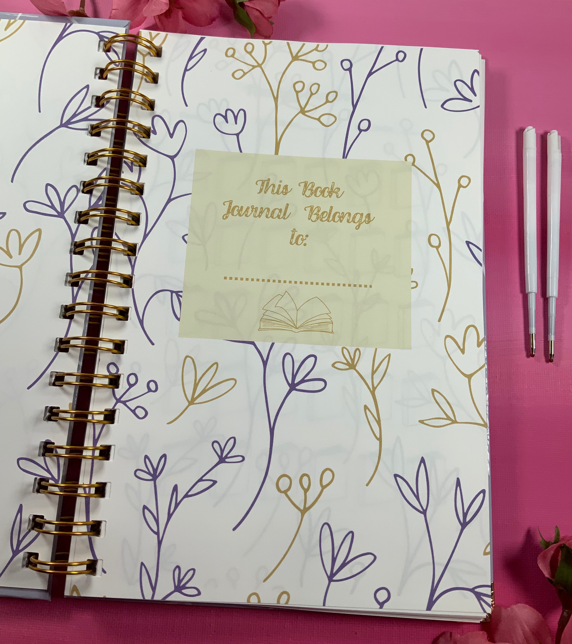 Journal with floral design and 'This Book Journal Belongs to' tag on a pink background