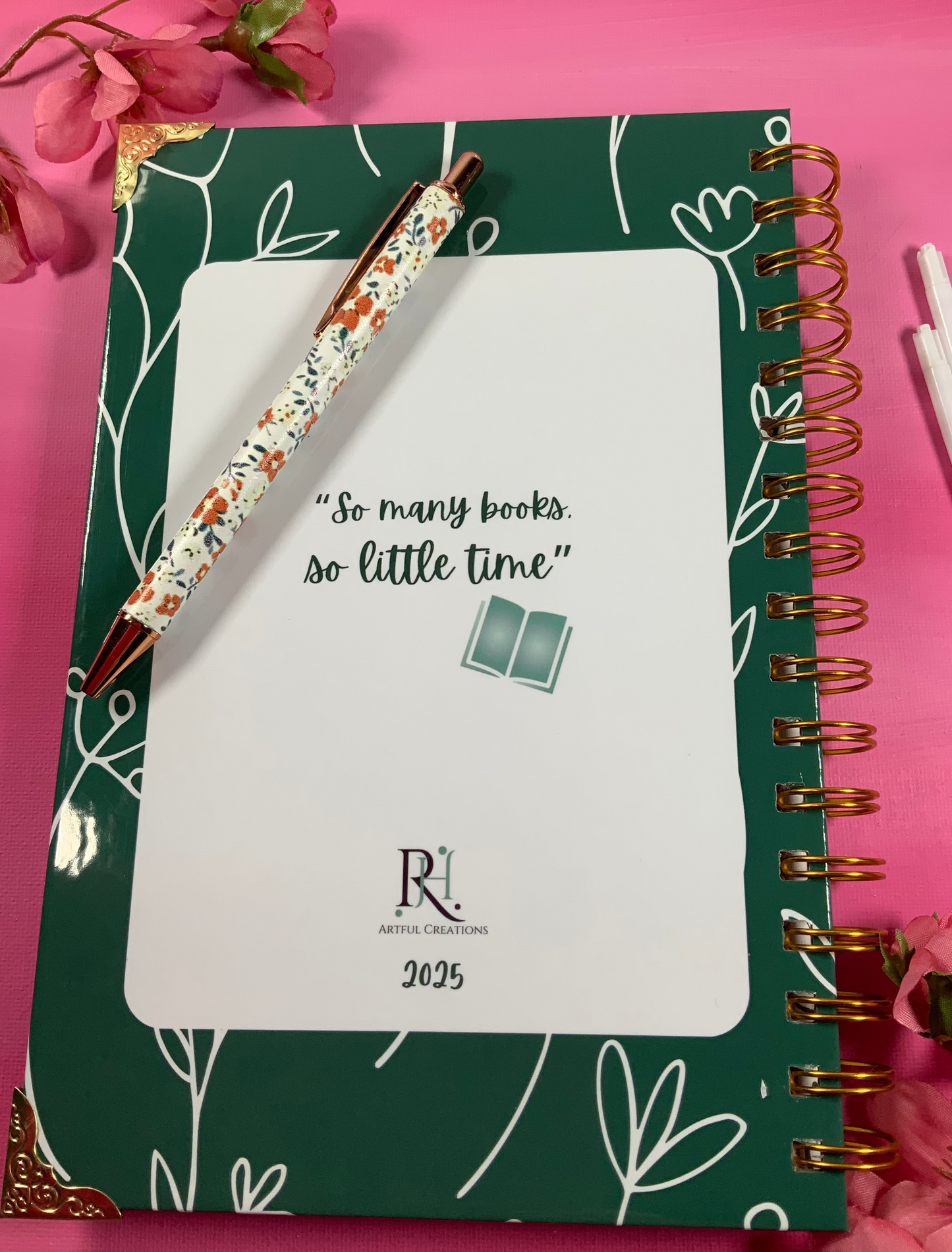 Green notebook with floral pen on a pink background