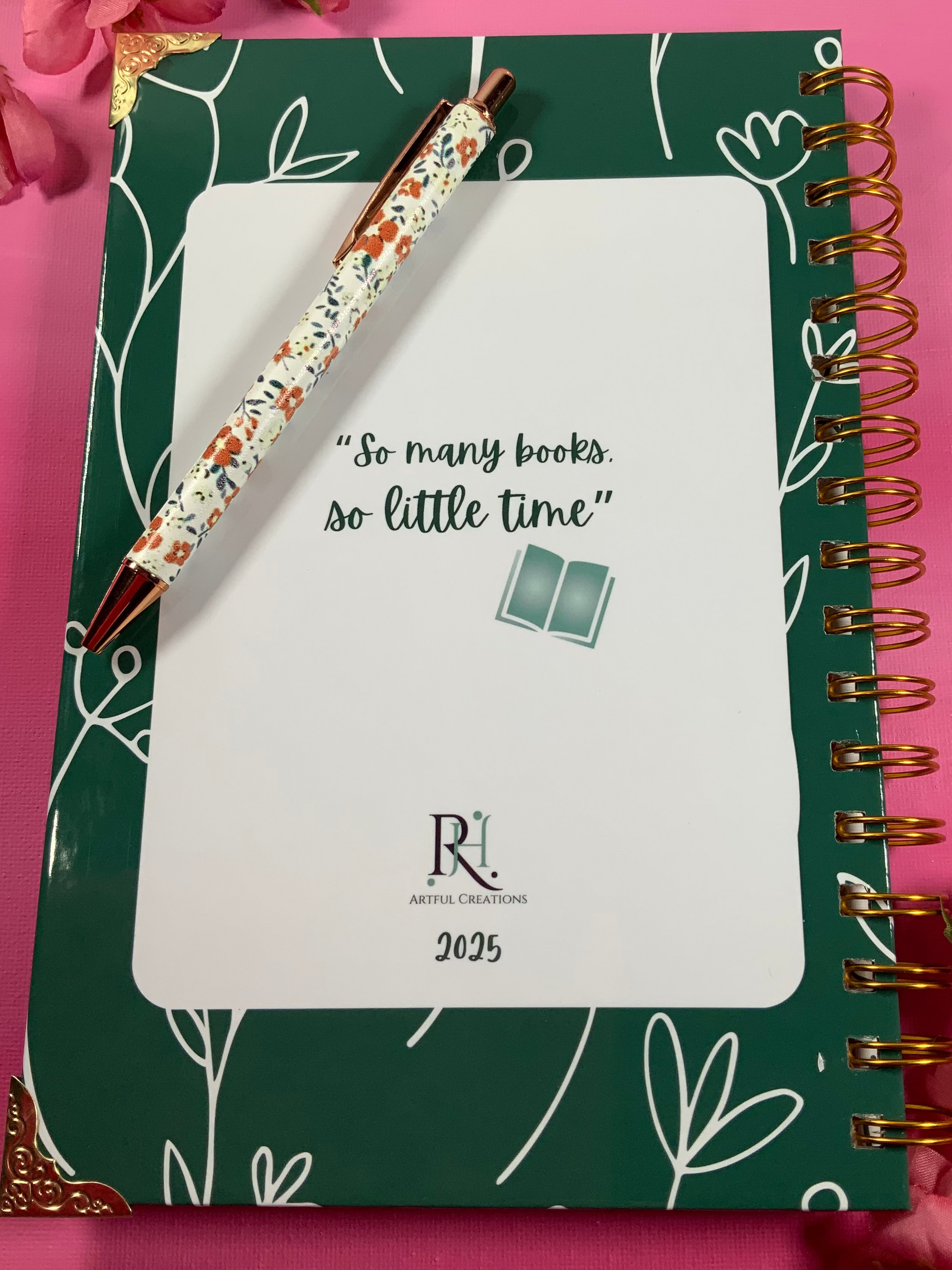 Green notebook with floral pen on a pink background