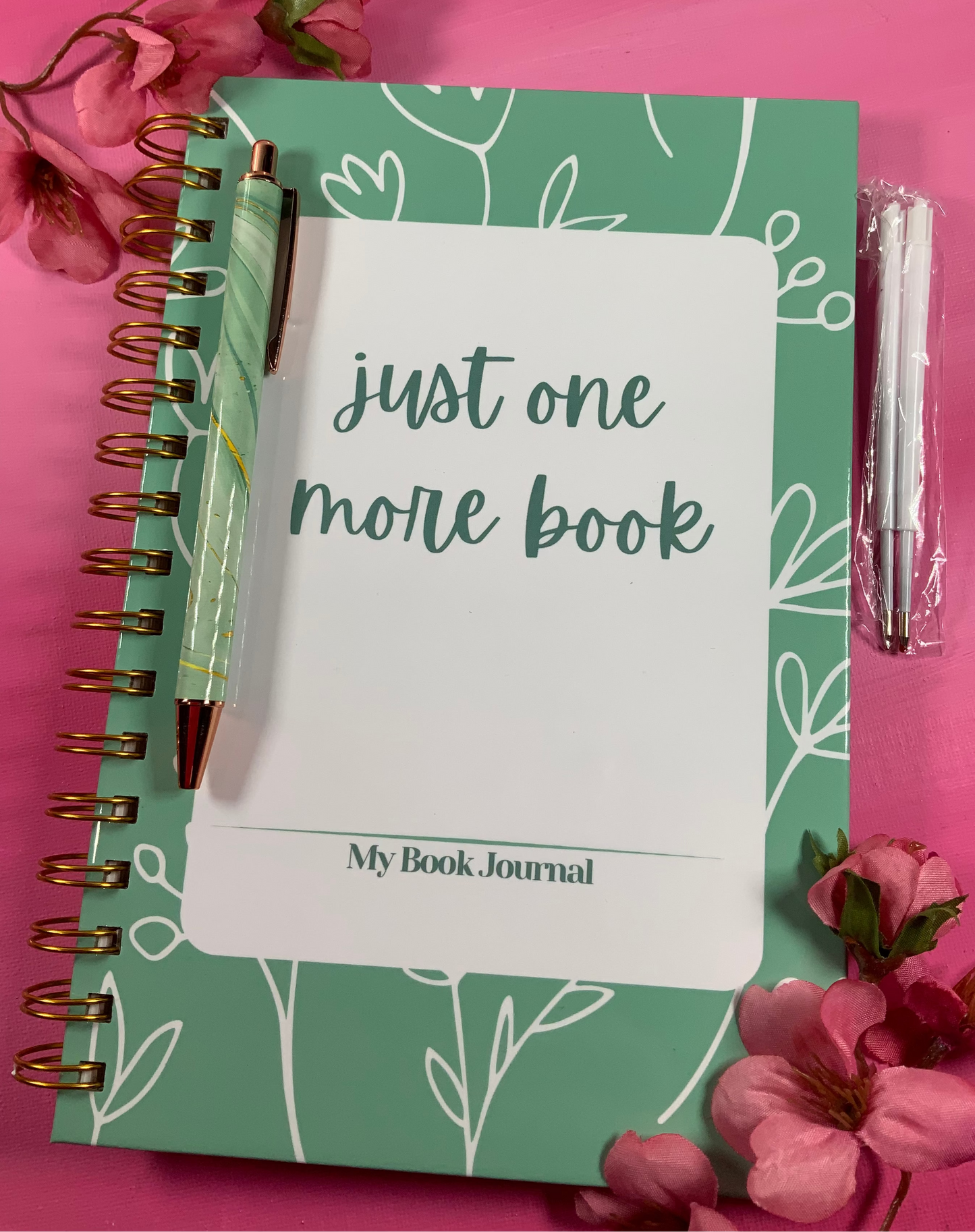 Green notebook with 'just one more book' text on a pink background
