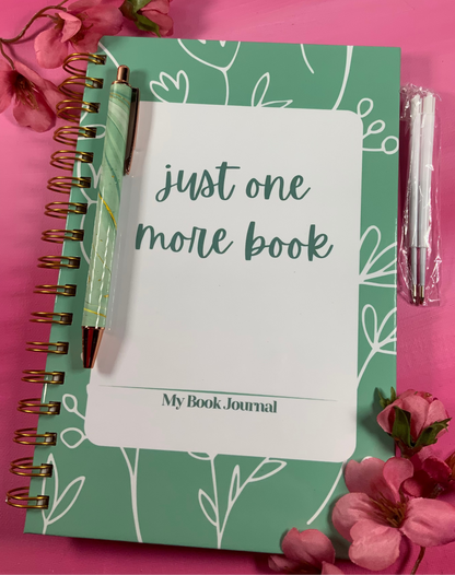 Green notebook with 'just one more book' text on a pink background