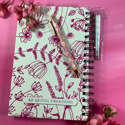 Notebook with floral design and pen on a pink background