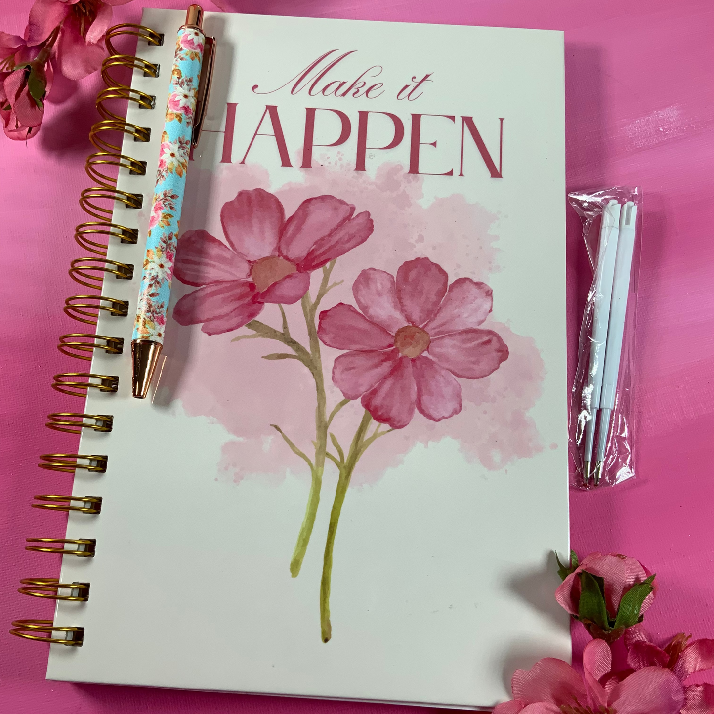 Notebook with floral design and 'Make it Happen' text on a pink background