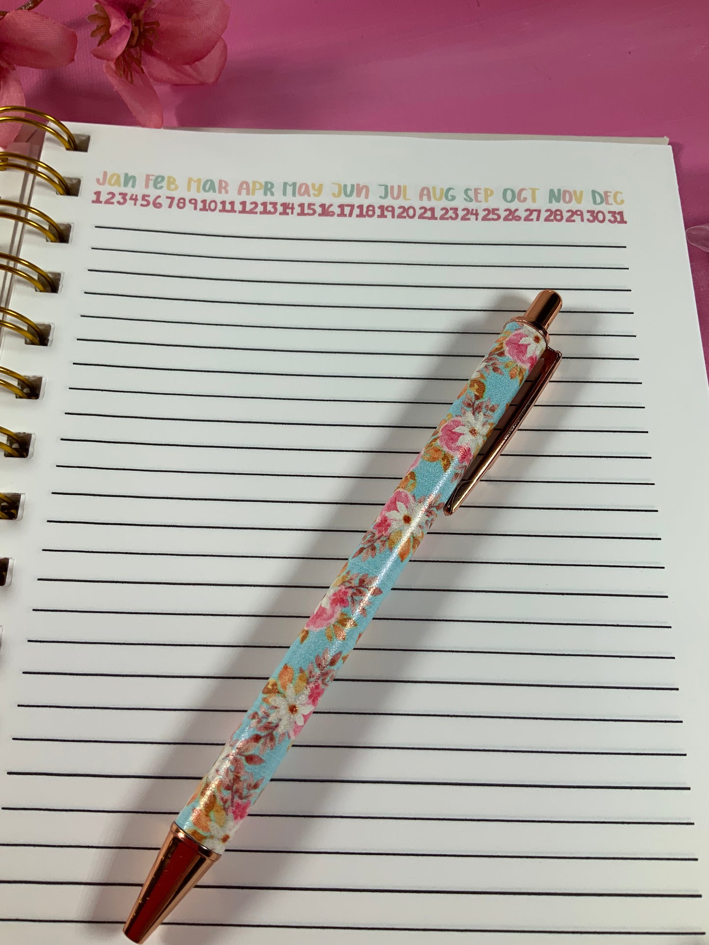 Floral-patterned pen on a lined notebook with a pink background