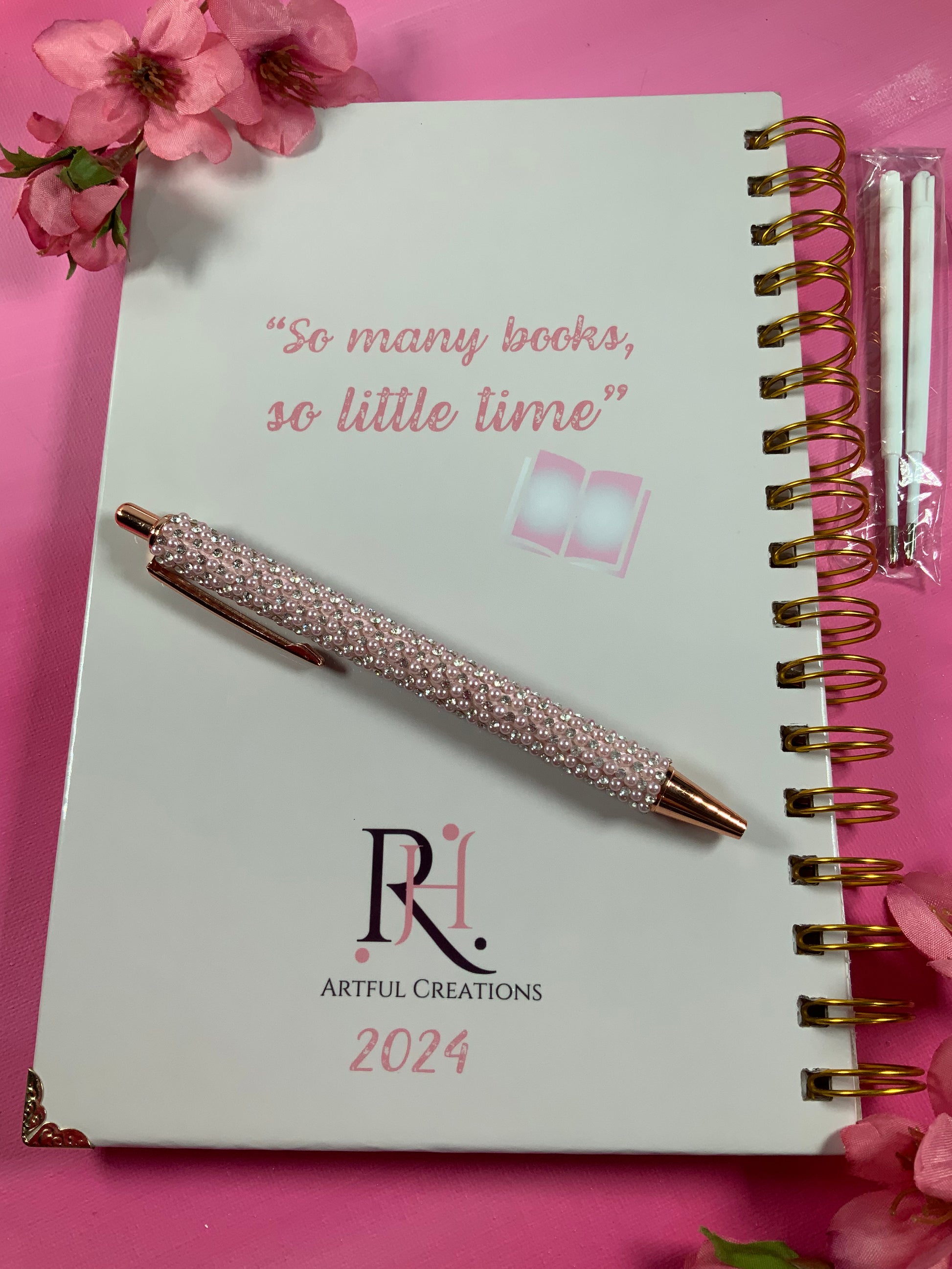 Spiral-bound notebook with a decorative pen on a pink background