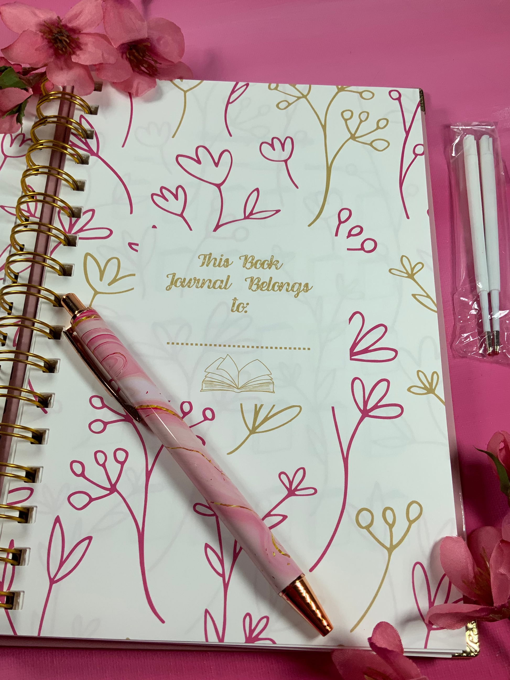 Notebook with floral design, pen, and cherry blossoms on a pink background