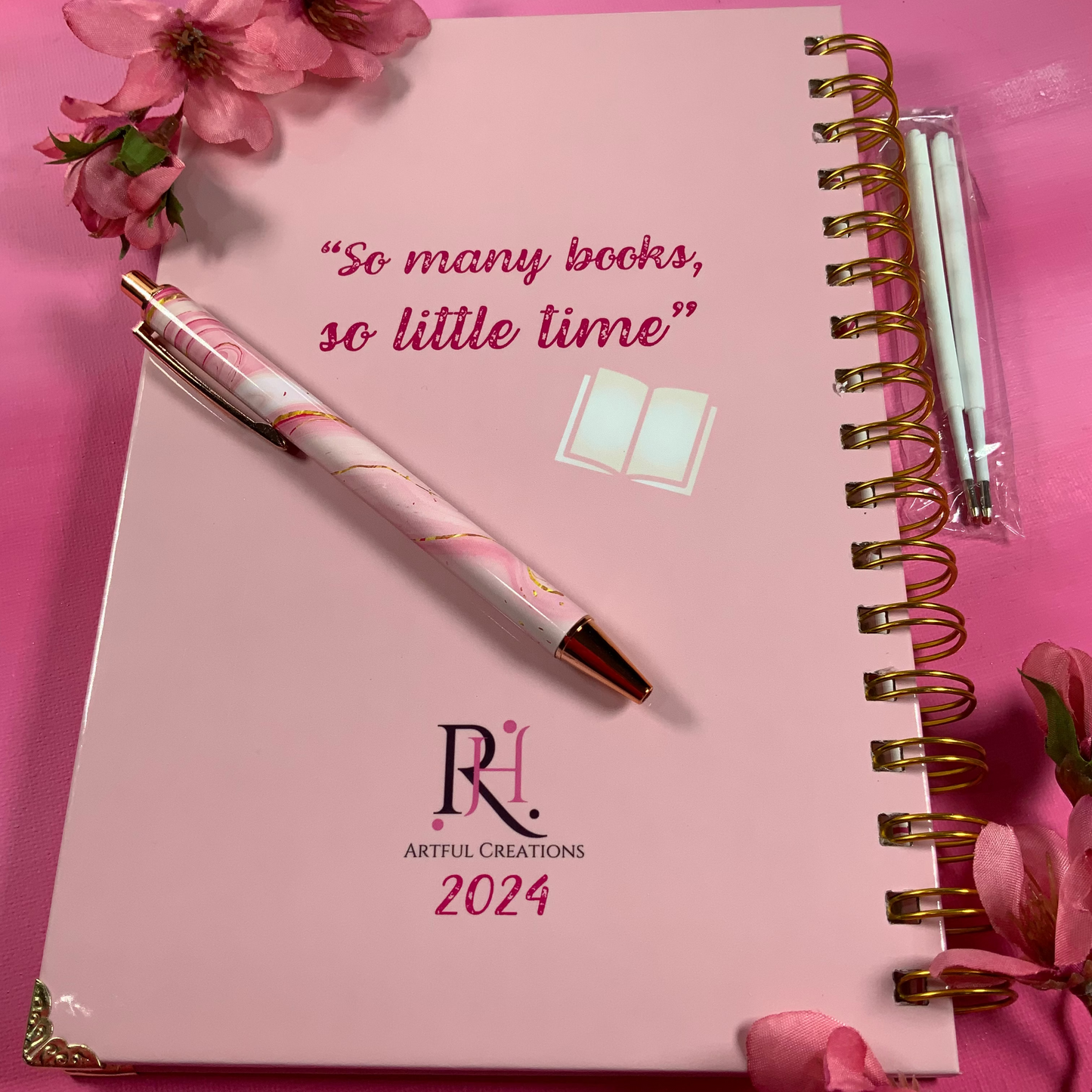 Pink planner with a pen and flowers on a pink background, featuring 'Artful Creations 2024' branding.