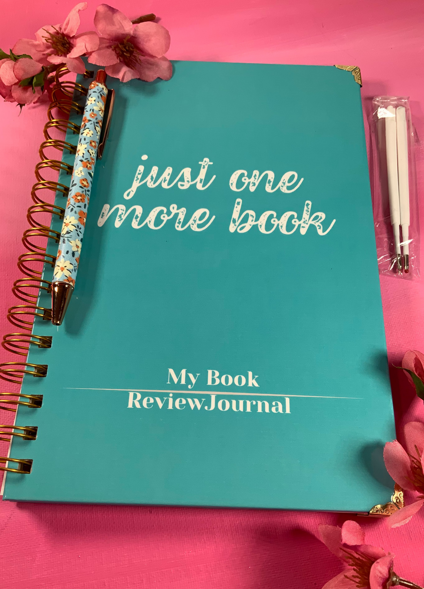 Turquoise notebook titled 'My Book Review Journal' on a pink background with flowers and a pen.