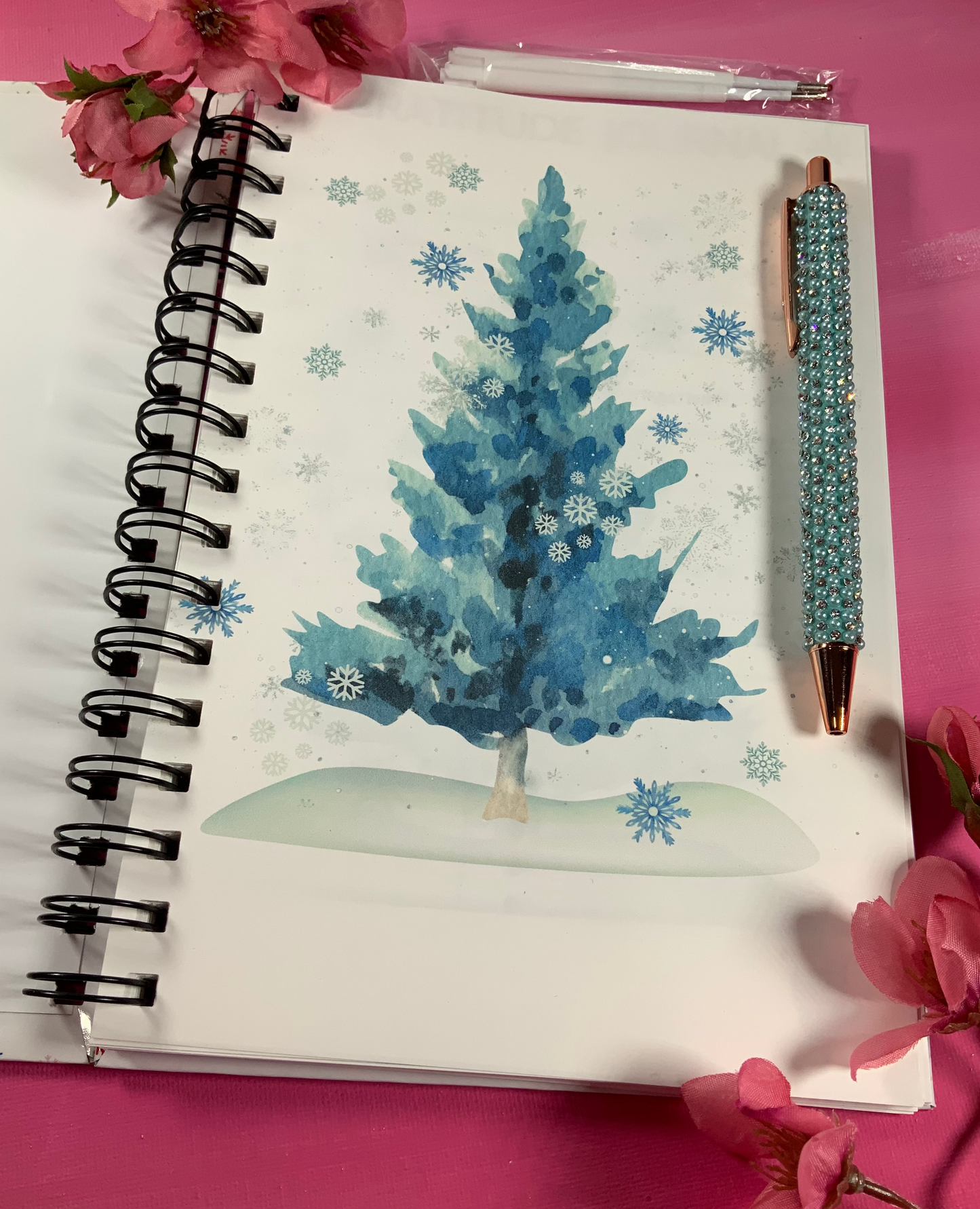Notebook with a blue Christmas tree illustration on a pink background