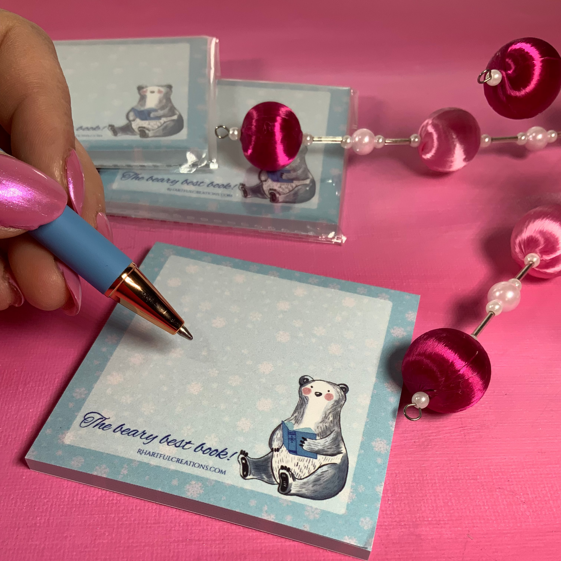 Notebook with bear illustration and pen on pink surface with decorative items