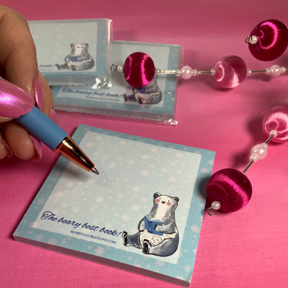 Notebook with bear illustration and pen on pink surface with decorative items