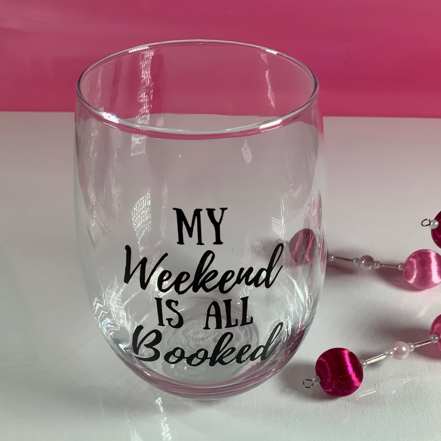 Clear glass with 'My Weekend is All Booked' text on a white surface with pink background
