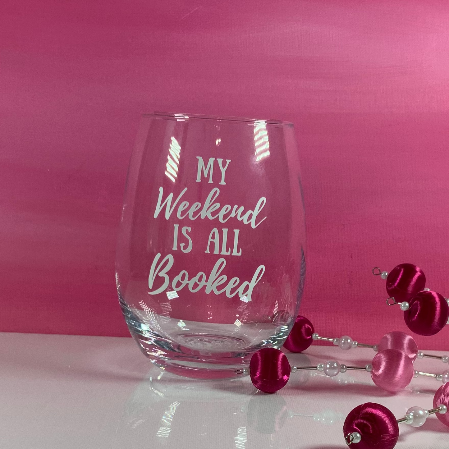 Stemless wine glass with 'My Weekend is All Booked' text on a pink background