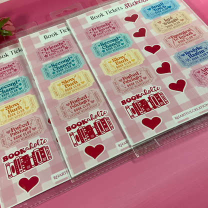 Sheet of book ticket stickers with colorful text and hearts on a pink surface