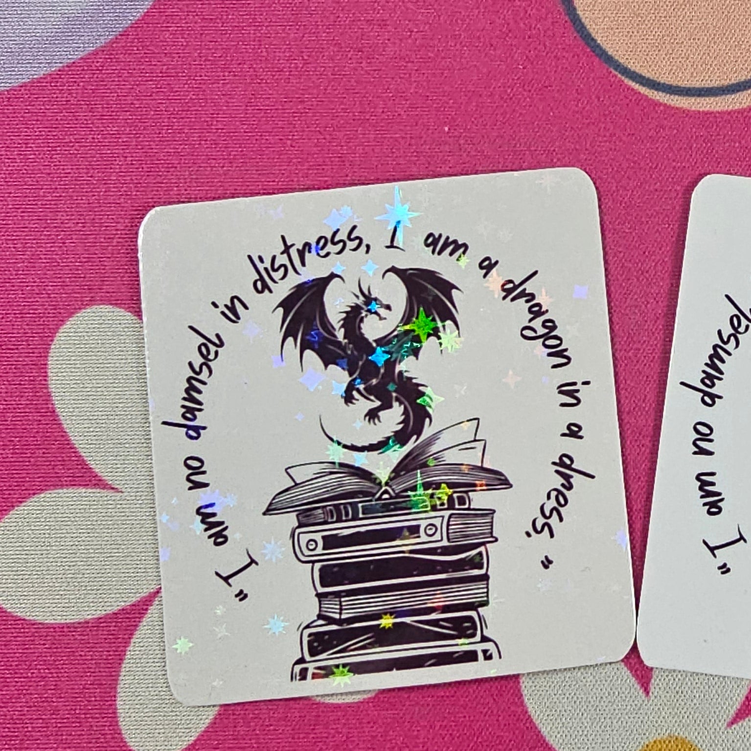 “I am no damsel in distress, I am a dragon in a dress” sticker featuring a black dragon sitting atop stacked books handmade by RH Artful Creations.