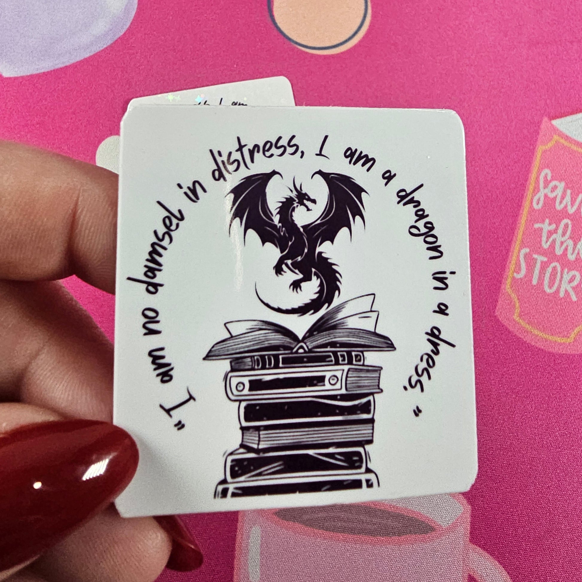 “I am no damsel in distress, I am a dragon in a dress” sticker featuring a black dragon sitting atop stacked books, handmade by RH Artful Creations.