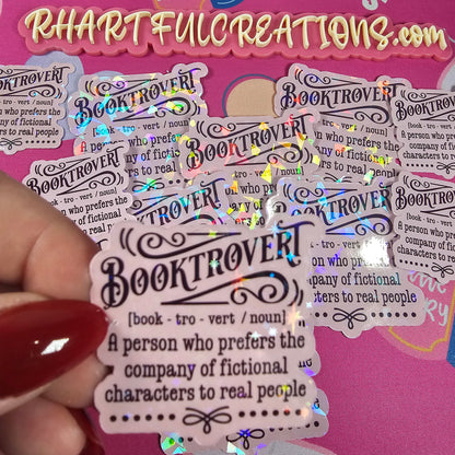 Sticker with 'Booktrover' definition held by a hand against a pink background with text and book illustrations.