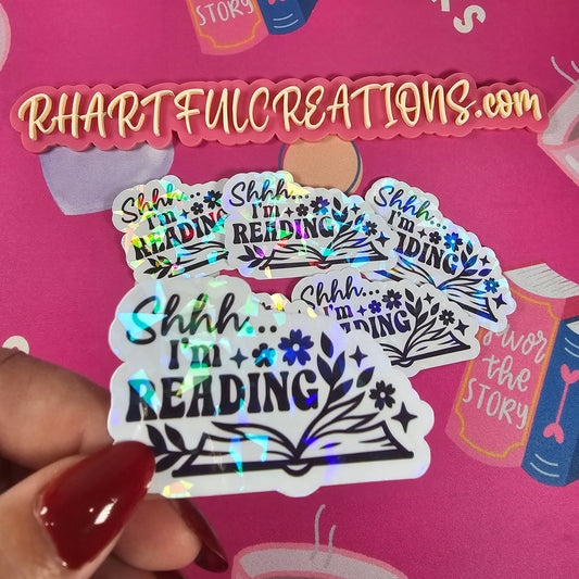 Holographic 'I'm Reading' stickers held in front of a pink background with book-themed designs.