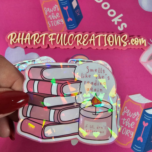 Holographic sticker of pink book stack with candle reading “if lit, don’t bother me” and text “Smells like she’s reading again,” handmade by RH Artful Creations.