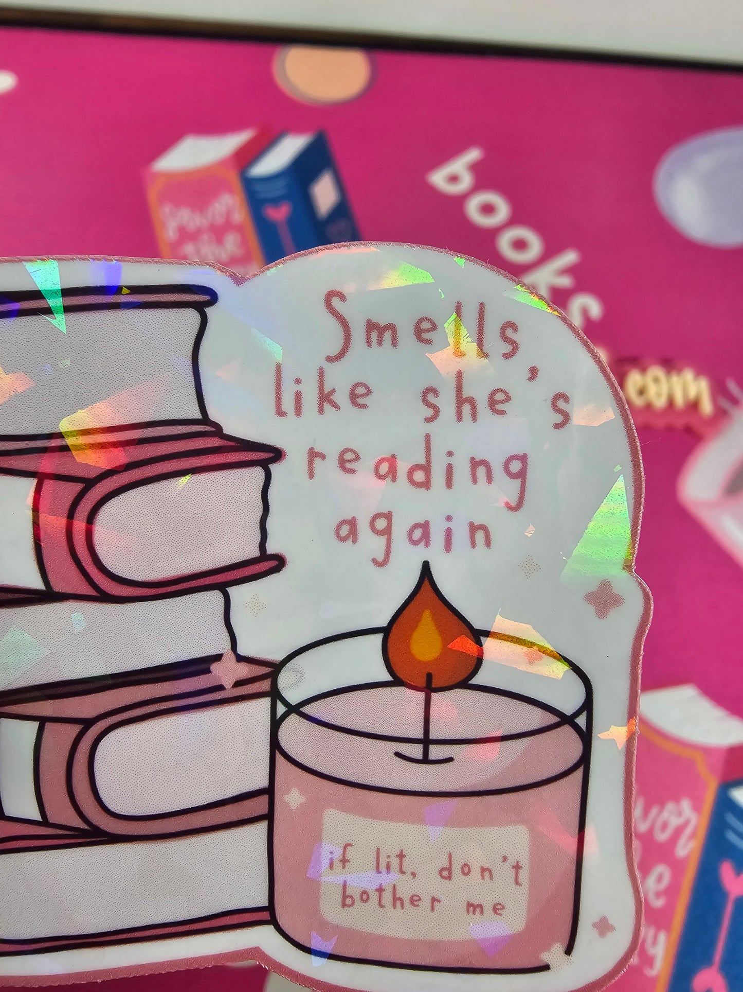 Holographic sticker of pink book stack with candle reading “if lit, don’t bother me” and text “Smells like she’s reading again,” handmade by RH Artful Creations.