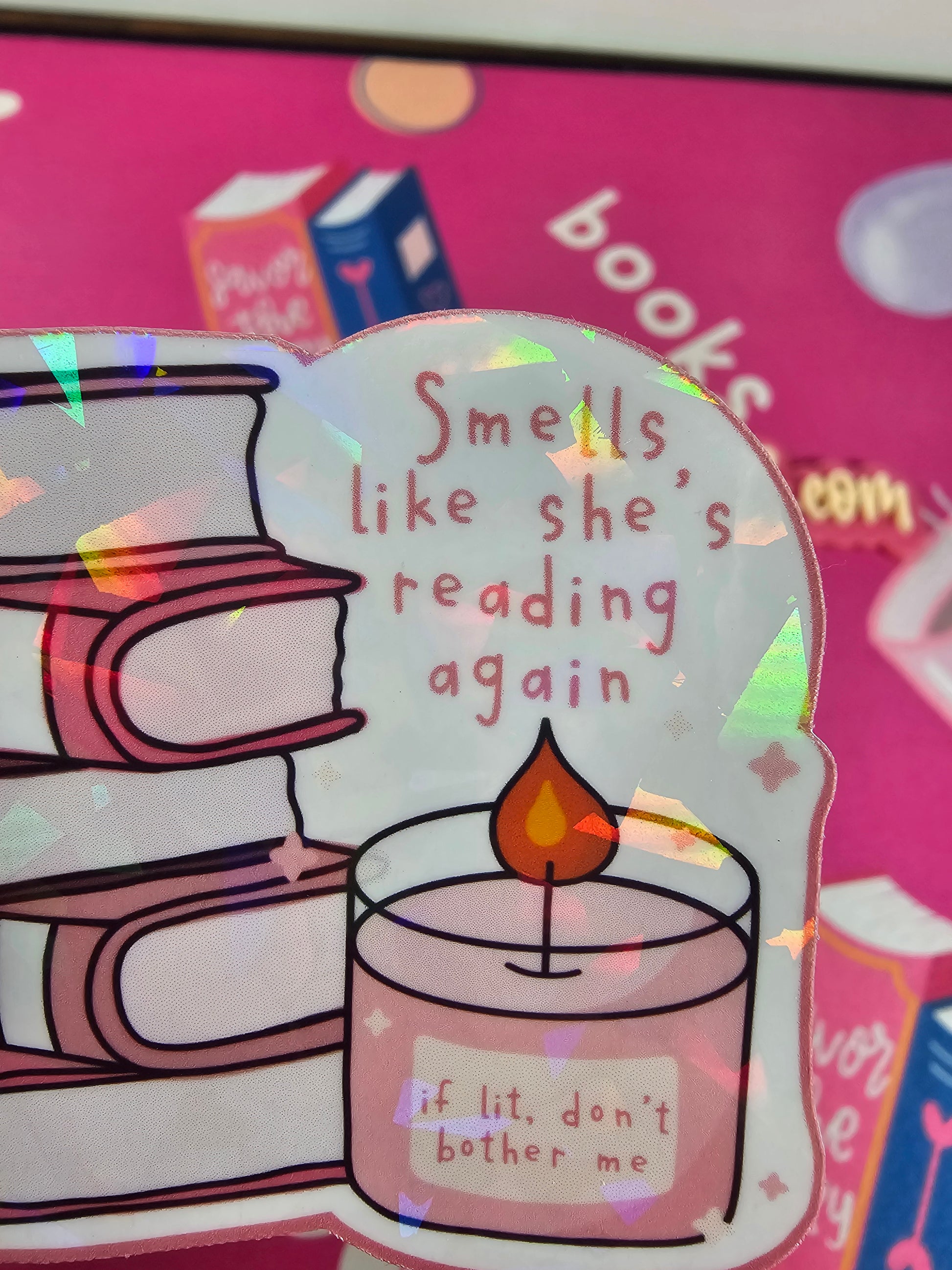 Holographic sticker of pink book stack with candle reading “if lit, don’t bother me” and text “Smells like she’s reading again,” handmade by RH Artful Creations.