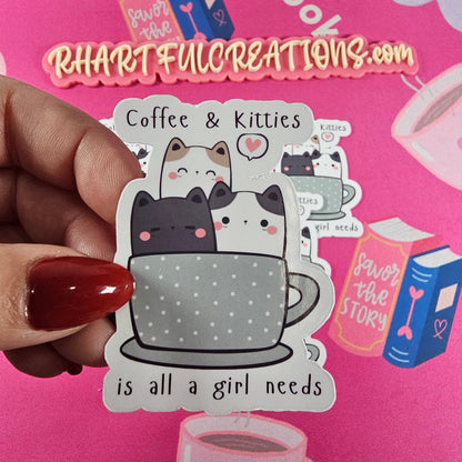Sticker with two cute cats sitting in a gray polka-dot coffee cup with the phrase “Coffee & Kitties is all a girl needs.”