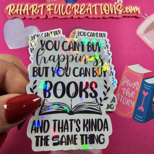 Sticker with text 'You can't buy happiness but you can buy books and that's kinda the same thing' held by a hand with red nail polish against a pink background.